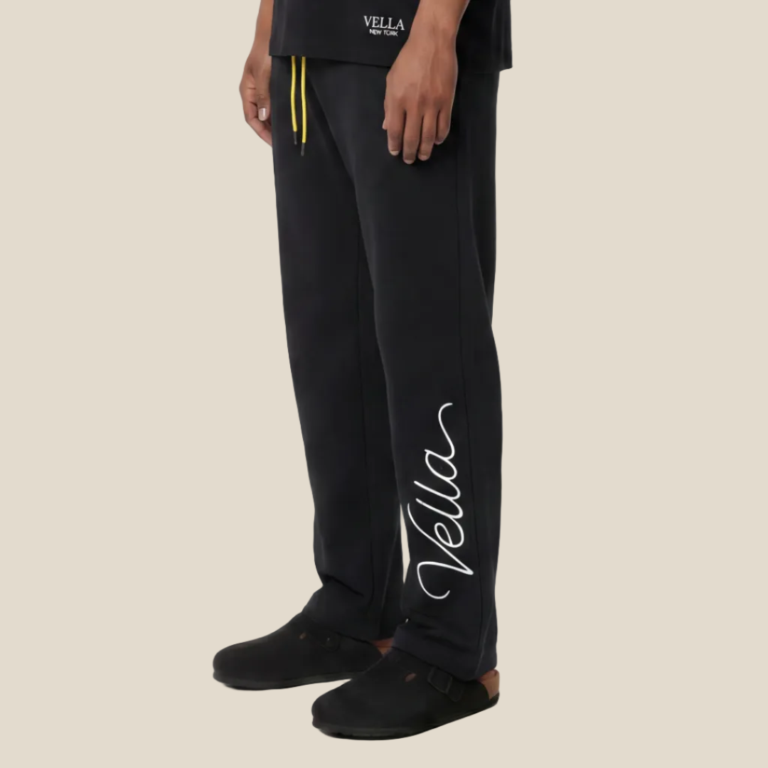 Man wearing a black t-shirt and pants with text on a offwhite background
