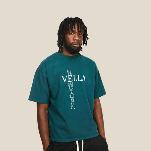 Person wearing a teal t-shirt with 'VELLA' branding on a plain background