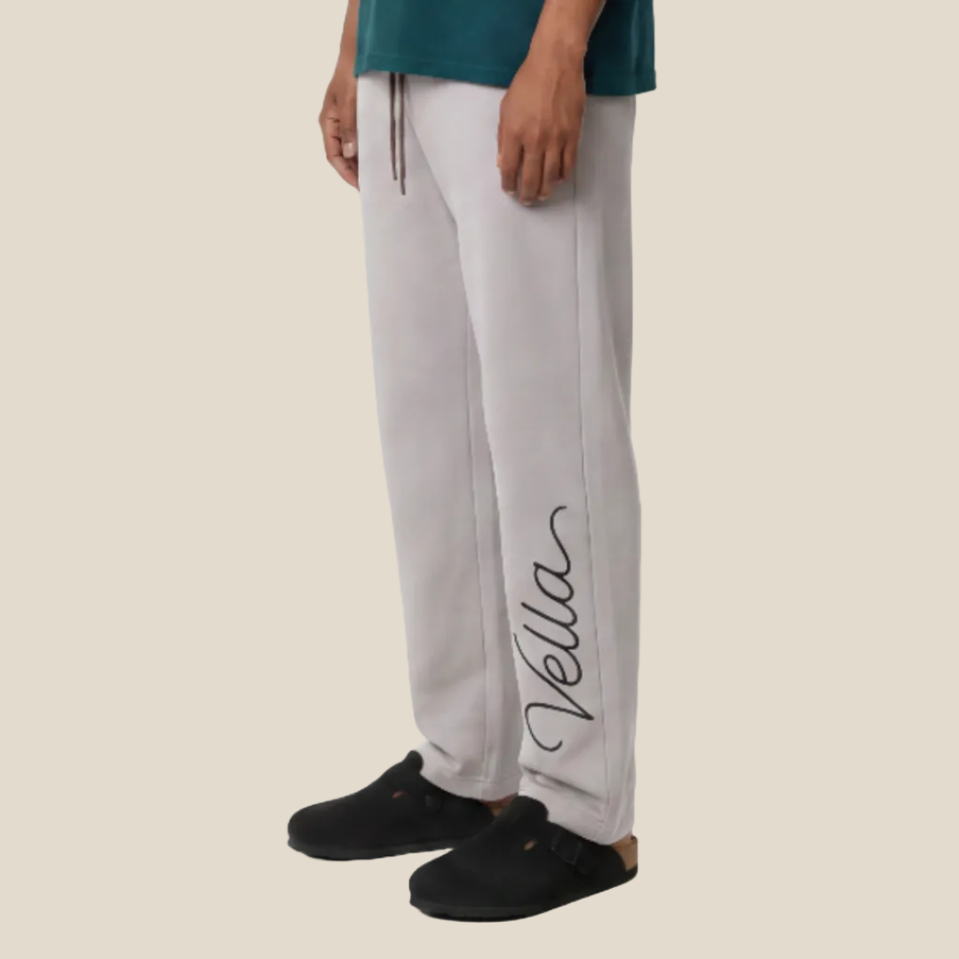 Man wearing a teal t-shirt and gray pants with 'Vella' branding on a white background